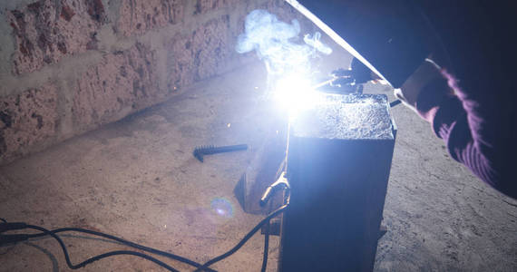 Welder performs welding work on metal in protective mask. 