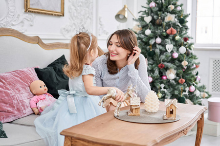 开朗的妈妈抱着她可爱的小女儿。家长和小孩在室内的圣诞树附近玩得很开心。圣诞快乐，新年快乐