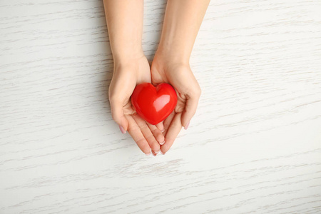 白色木质背景上红色心形的女性手。心脏病学概念