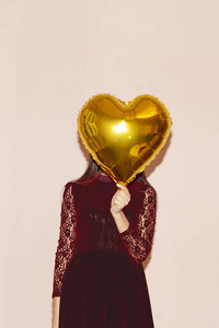 女人用心形的金色气球遮住脸。情人节，生日，妇女节，周年纪念，节日庆祝概念