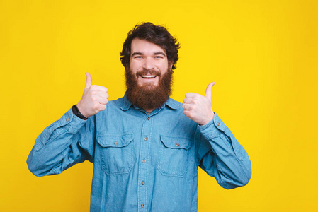 快乐的大胡子男人穿着蓝色衬衫在黄色背景上竖起大拇指