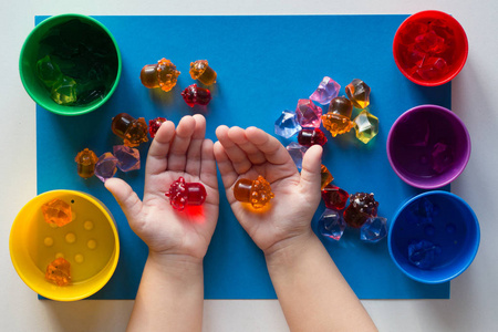 儿童手拿五颜六色的玩具，在蓝色表面按颜色分为五颜六色的杯子