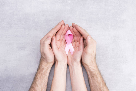 保健和医学概念女性和男性手拿着灰色背景的粉红色乳腺癌意识丝带