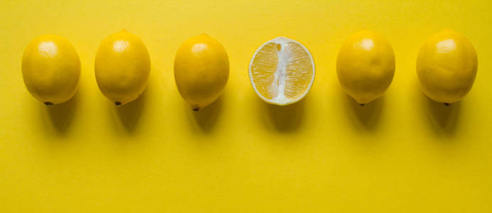 俯视图完整切片的成熟柠檬在黄色表面上一字排开，健康和维生素的概念