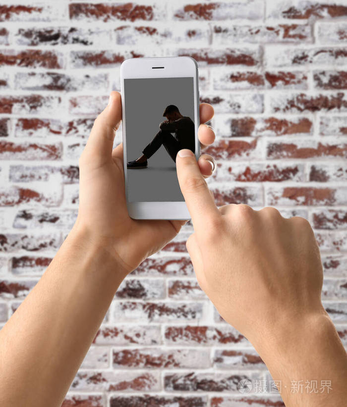 手拿手机与沮丧的年轻人在屏幕上靠着砖墙