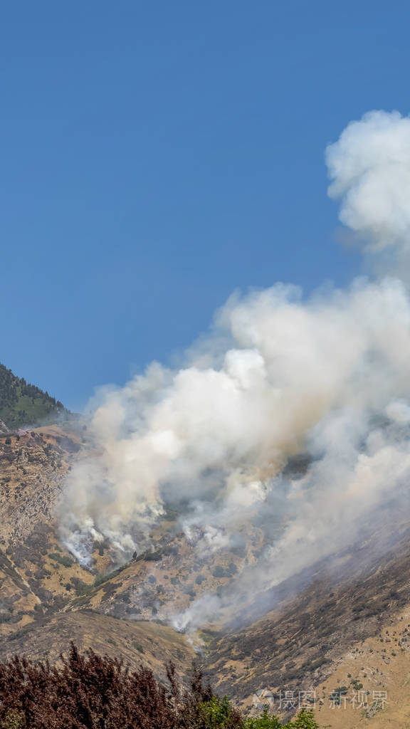 在清澈的蓝天背景下山上从火中喷出的垂直浓烟