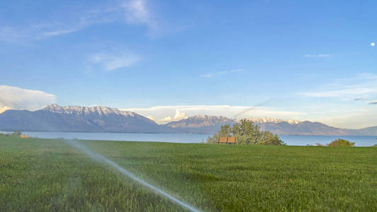 全景式喷灌机以风景自然景观为背景，在绿草上喷水