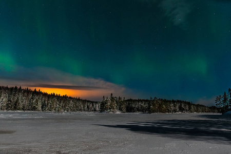 戏剧性的极光，极光与许多云和星星在月光下的天空在冻结的湖泊和雪林瑞典。长快门速度。