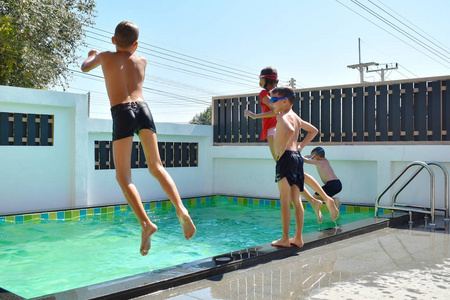 一群孩子跳进游泳池。快乐的孩子们在房子的私人游泳池里游泳。度假胜地的暑假。