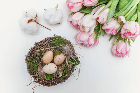 复活节彩蛋在巢与苔藓棉花和粉红色新鲜郁金香花束