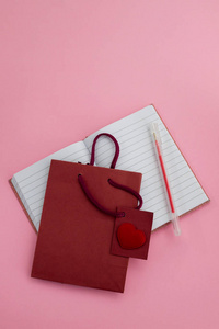 心与小纸袋和笔记本与钢笔在粉红色的背景