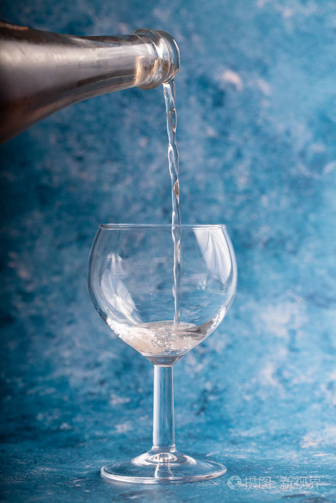 酒倒在蓝色背景的玻璃杯上