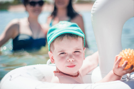 一个戴着蓝色棒球帽的可爱小男孩戴着一个充气环在海里游泳。