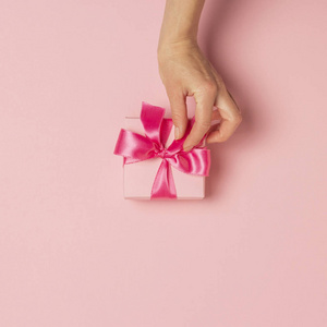 女性手拿着，拿着，收到粉红色背景的礼物。婚礼概念，情人节，送给爱人的礼物。平放，俯视图