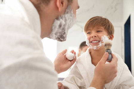 爸爸在浴室把剃须泡沫涂在儿子的脸上