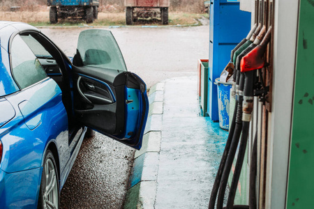 蓝色汽车停在加油站加油。多雨，寒冷的天气