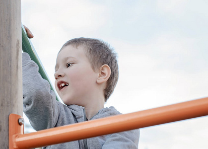Happy boy climbing on children playground outdoors. 