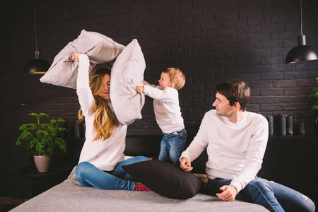 父母带着微笑的孩子在床上玩枕头大战,快乐的家庭在卧室里玩耍,享受