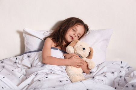 爱与梦想小可爱的孩子躺在床上,闭上眼睛,酣睡,做梦,抱着她的泰迪熊
