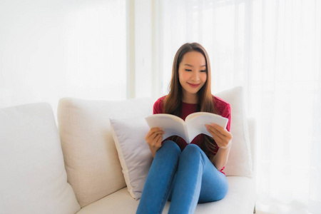 美丽的亚洲年轻女性在沙发椅上看书
