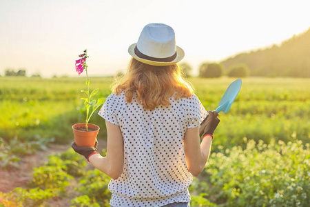 戴帽子戴手套的小女孩拿着铲子和花盆在花园里散步
