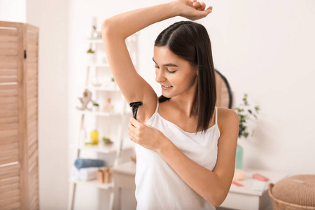 漂亮的年轻女人在浴室刮腋毛照片