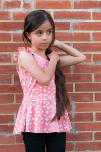 长发哥伦比亚女孩在砖墙旁整理头发