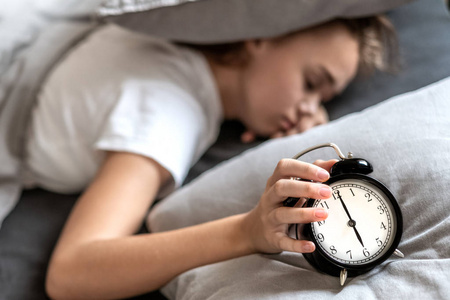 Woman with insomnia lying in bed with her head under her pillow 