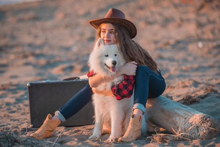 年轻萨摩耶一个戴着帽子的年轻漂亮女人坐在沙滩上拥抱一只白色的