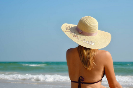 海滩上美丽的女孩。海中戴帽子的女人望着远方。