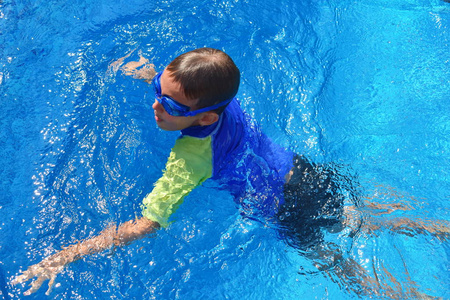 旅馆里蓝色游泳池里的男婴。孩子戴着护目镜游泳