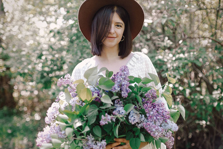 时髦的波西米亚女人戴着帽子，在阳光下捧着淡紫色的花束