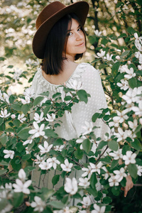 时髦的波西米亚女人戴着帽子，在盛开的树上摆出白色的花