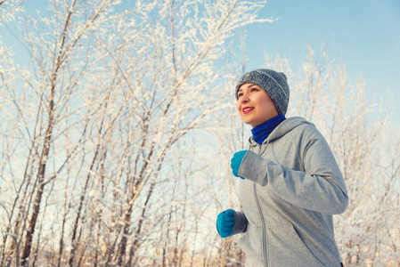 跑步女运动员。穿着保暖运动服和手套的女跑步者在寒冷的冬季森林里慢跑。