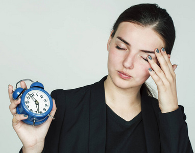 身着商务装的年轻美女清晨在白色背景下手持闹钟起床上班照片