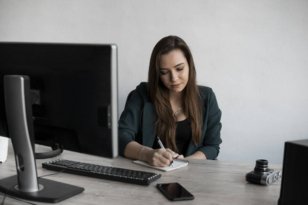 女商人在笔记本上写东西。创业女企业家学生在工作场所靠近电脑学习写笔记。一个女人在桌上一个白色的空白笔记本上手写。