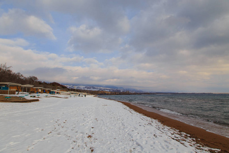 冬季海滩。碧蓝清澈的海水，沙滩上的雪。地平线和山脉。吉尔吉斯斯坦，伊塞克湖