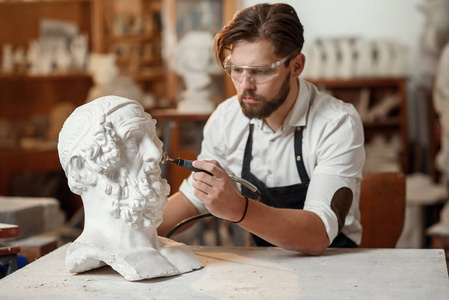 男雕塑家在创意艺术工作室的工作场所修复女性头部的石膏雕塑.照片