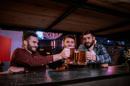 三个朋友在酒吧里喝着淡啤酒敬酒。美丽的背景