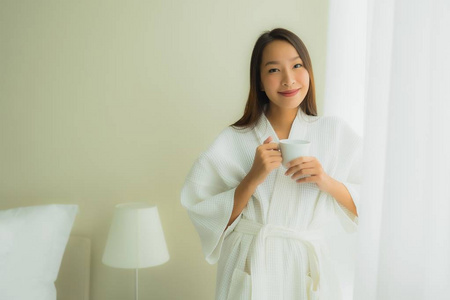 卧室里拿着咖啡杯的美丽的亚洲年轻女性肖像