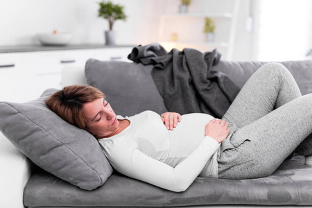 Pregnant tired exhausted woman with stomach issues at home on a 