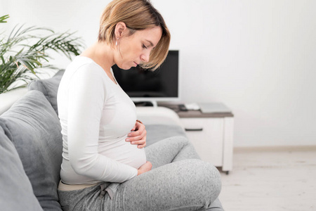 Pregnant tired exhausted woman with stomach issues at home on a 