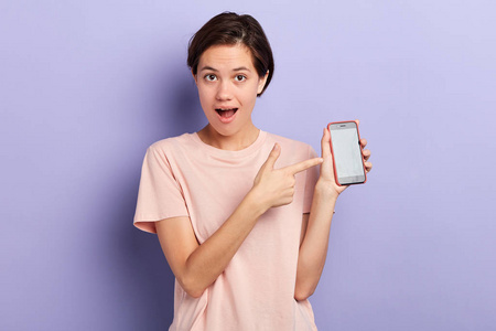 兴奋的美女指着蓝色背景的智能手机.照片