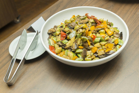 木制桌子上的白色陶瓷盘子里的美味蔬菜沙拉。切片黄胡椒，橄榄，晒干的西红柿和黄瓜。健康饮食理念。选择性聚焦。