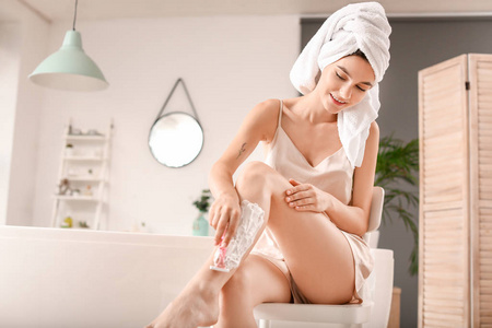 漂亮的年轻女人在浴室刮腿毛图片
