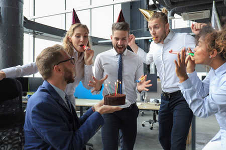 快乐的商务团队拿着生日蛋糕在办公室聚会上问候同事