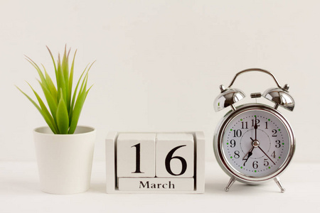 3月16日在木制日历上，旁边是一个闹钟和白色背景上的一朵花。一天的概念年。意义重大日期或事件