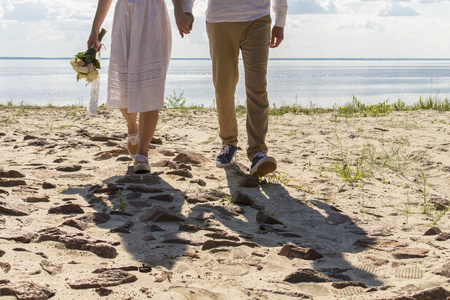 新婚夫妇手拿结婚花束沿着海滩散步