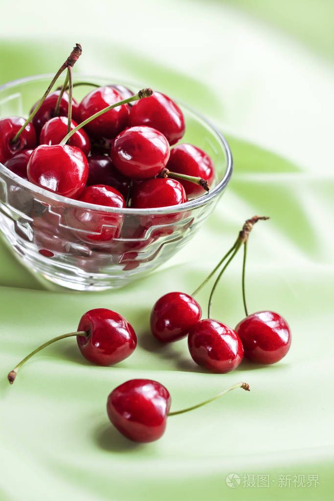多汁的成熟甜樱桃放在玻璃碗里背景是柔和的绿色布