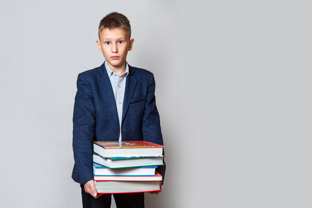 一个十几岁的男孩穿着蓝色的西装，灰色的背景上放着大本书。概念学习的复杂性，学习新事物。